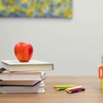 an apple on top of schoolbooks, with ABC blocks and colored pencils